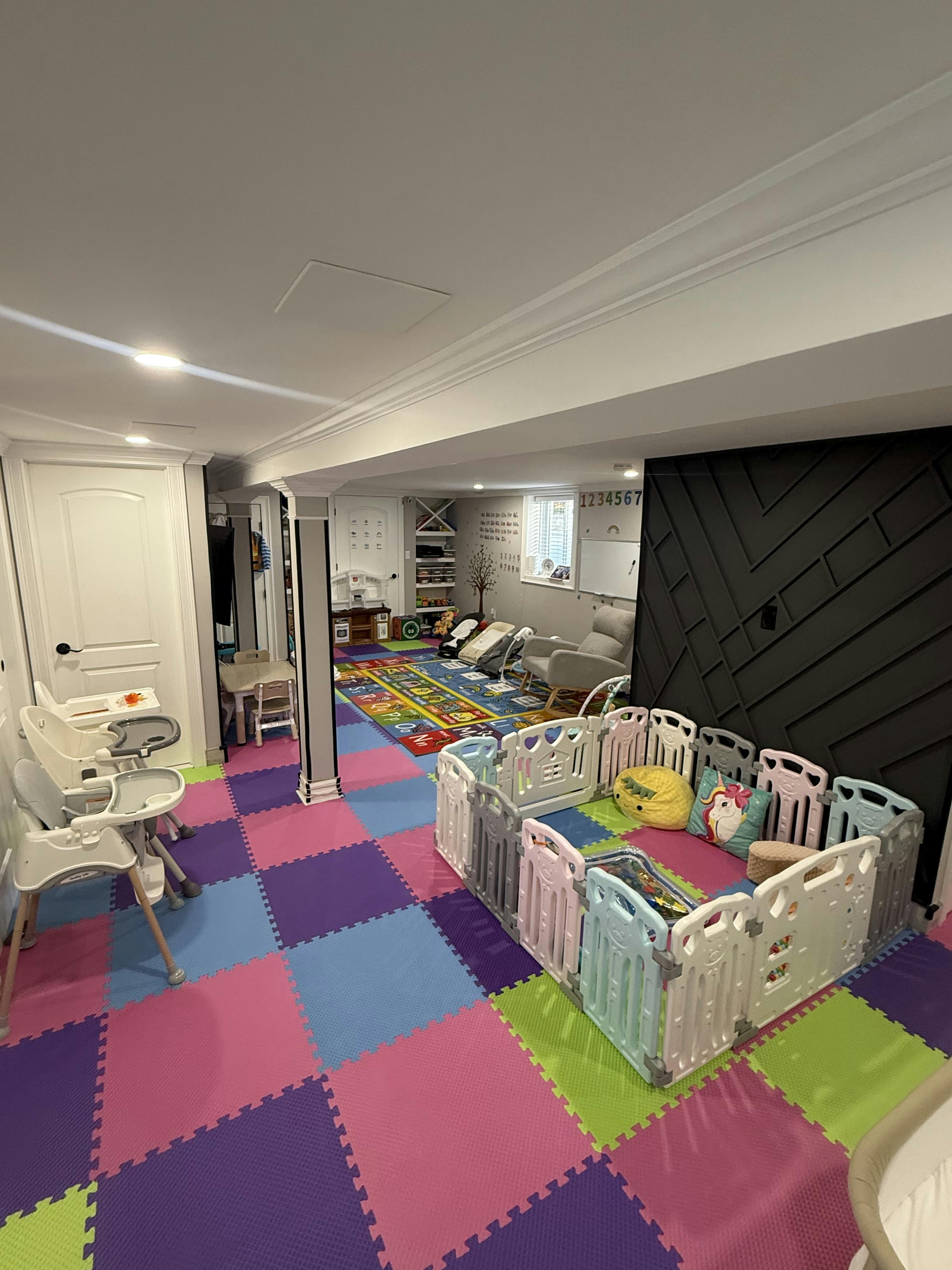 Childcare room with colorful floor mats, high chairs, and a playpen