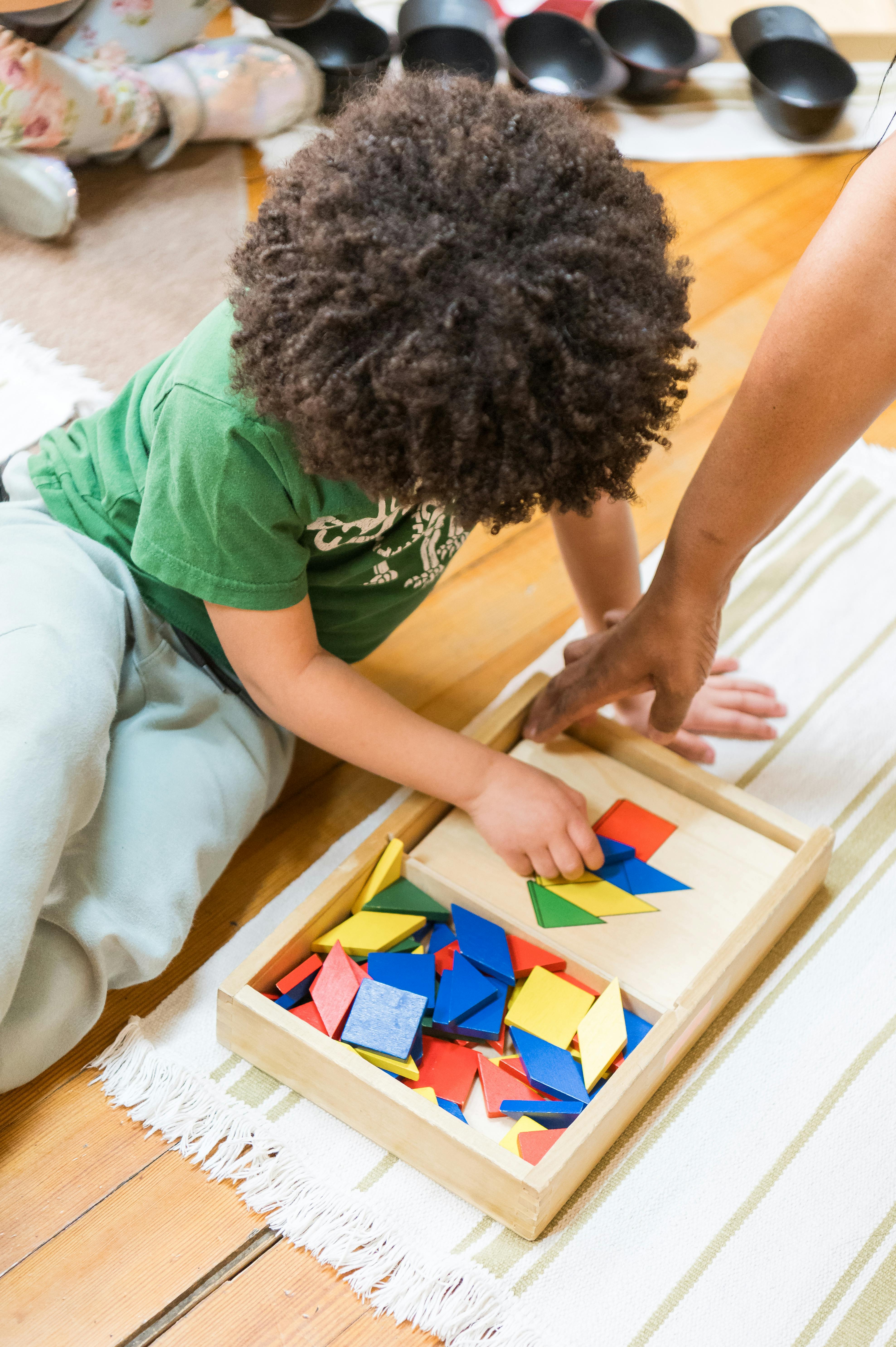 Child playing with colorful geometric shapes in a wooden tray