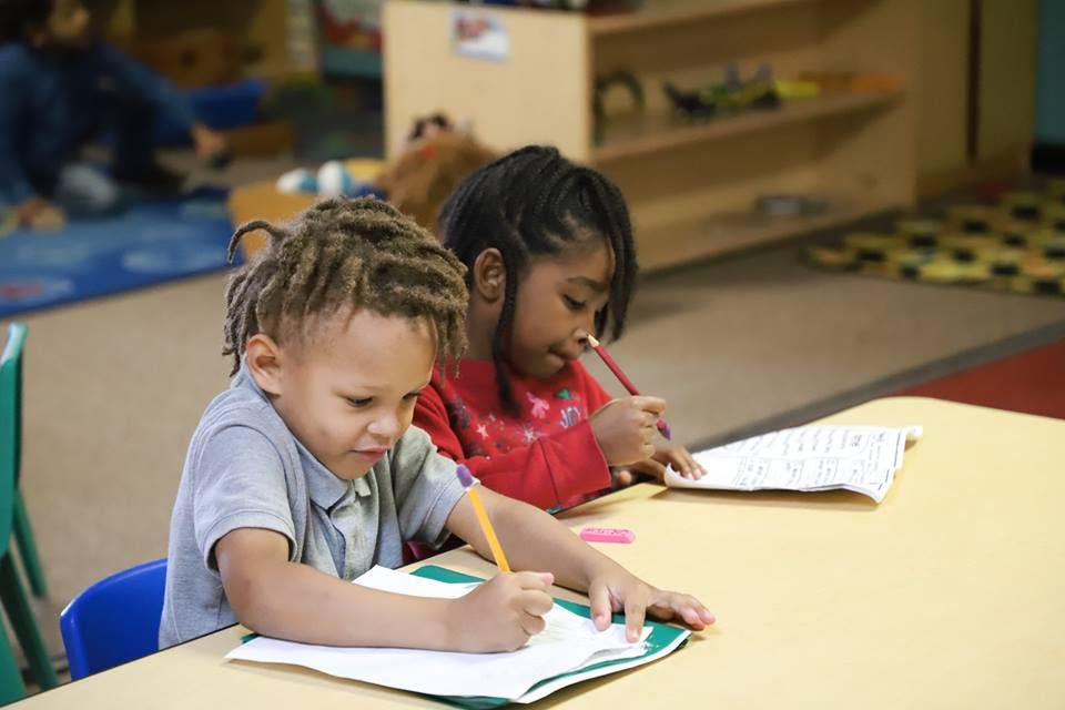 Two children writing at a table in a classroom