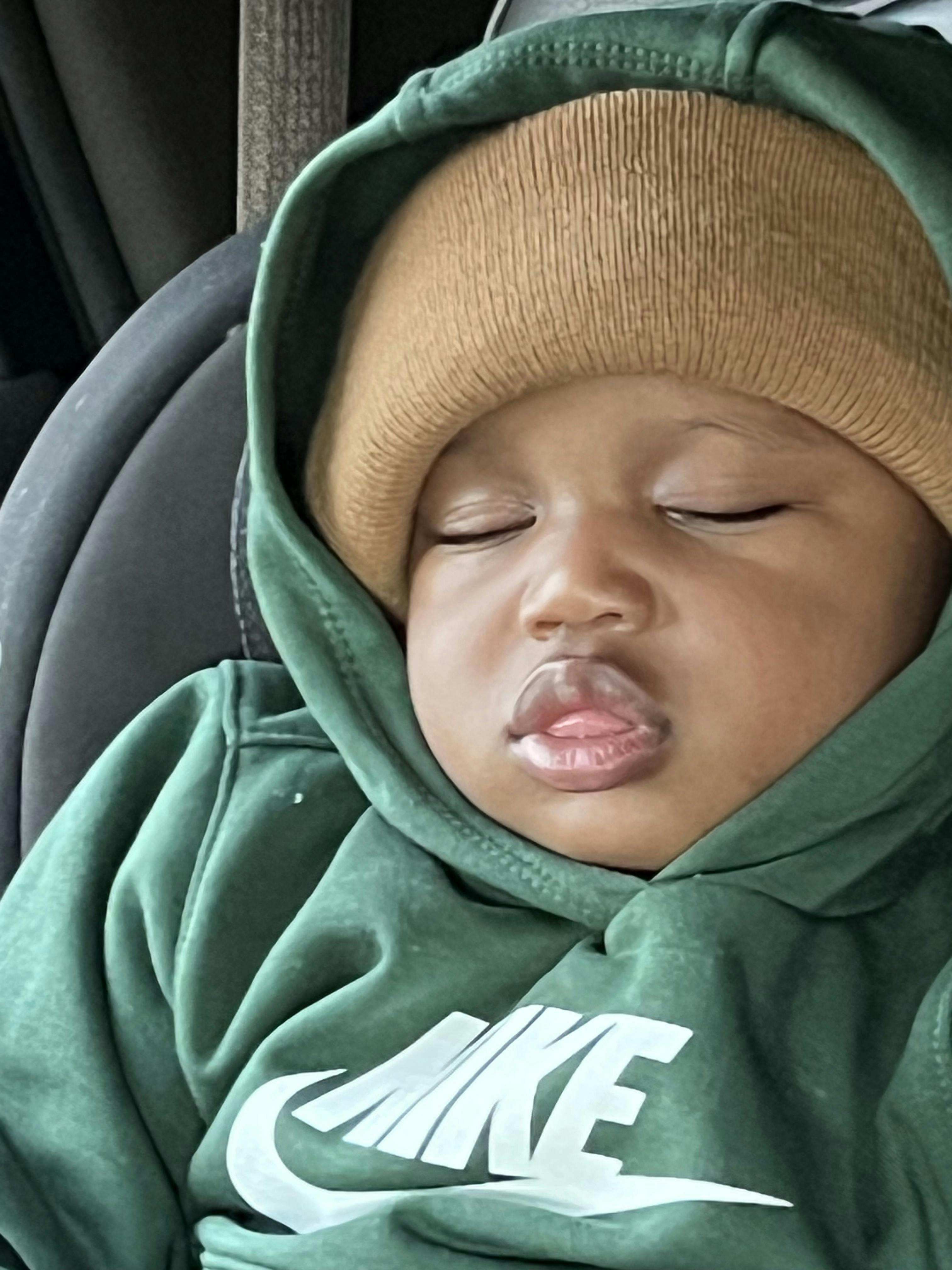 Child sleeping in a green hooded sweatshirt and a brown beanie