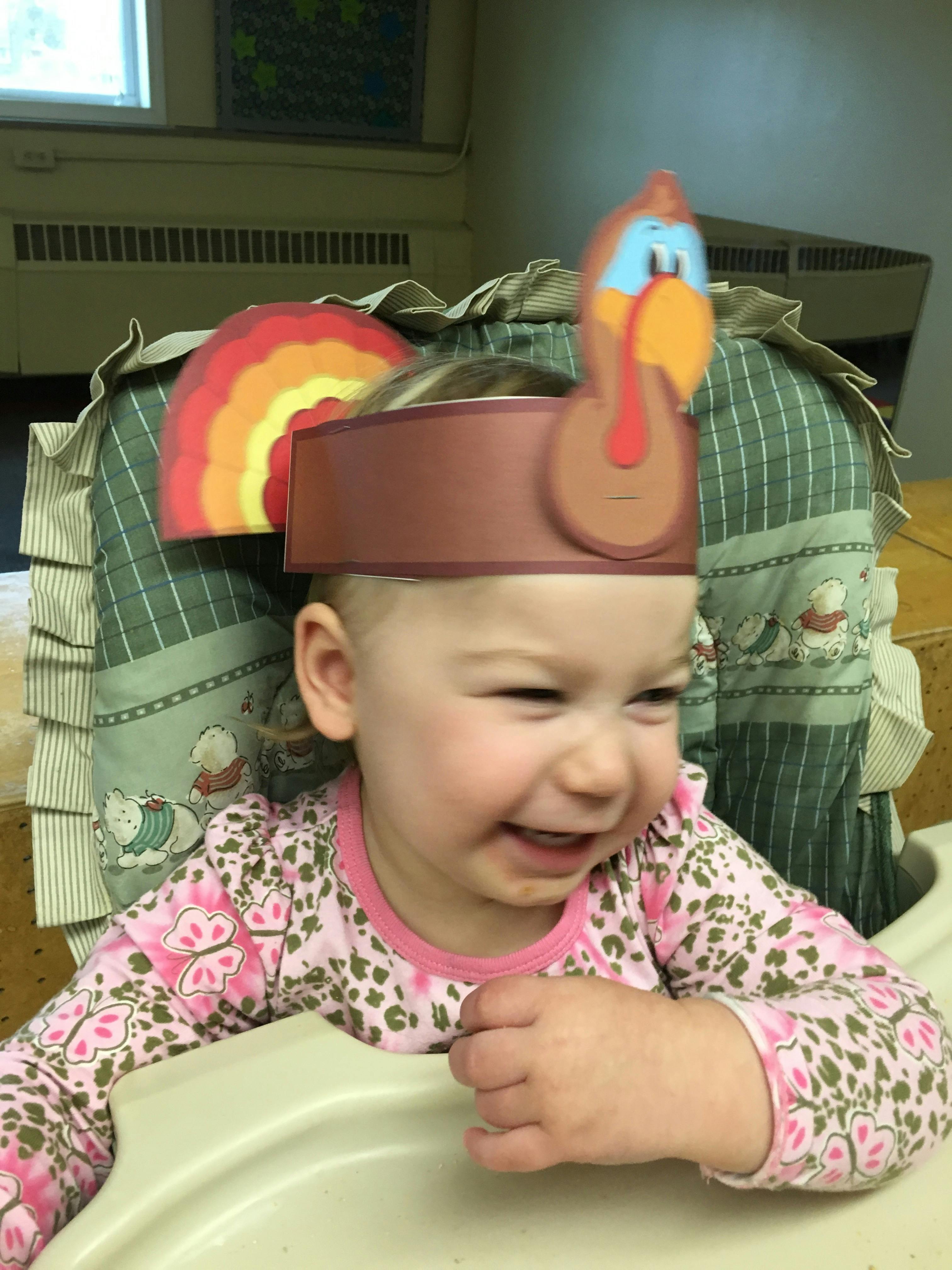 Child in a high chair wearing a turkey headband