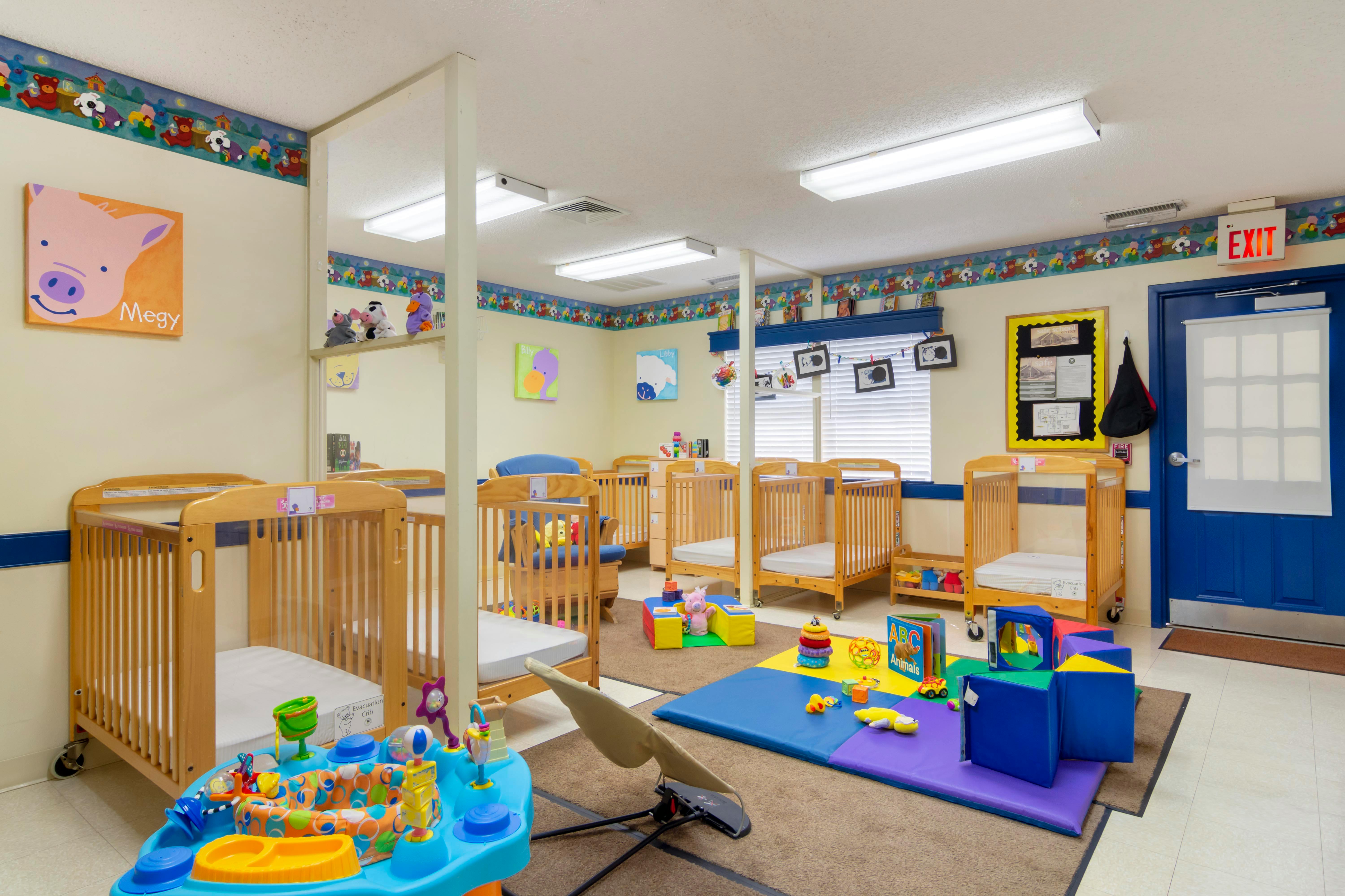 A brightly lit nursery room with multiple wooden cribs and colorful play mats