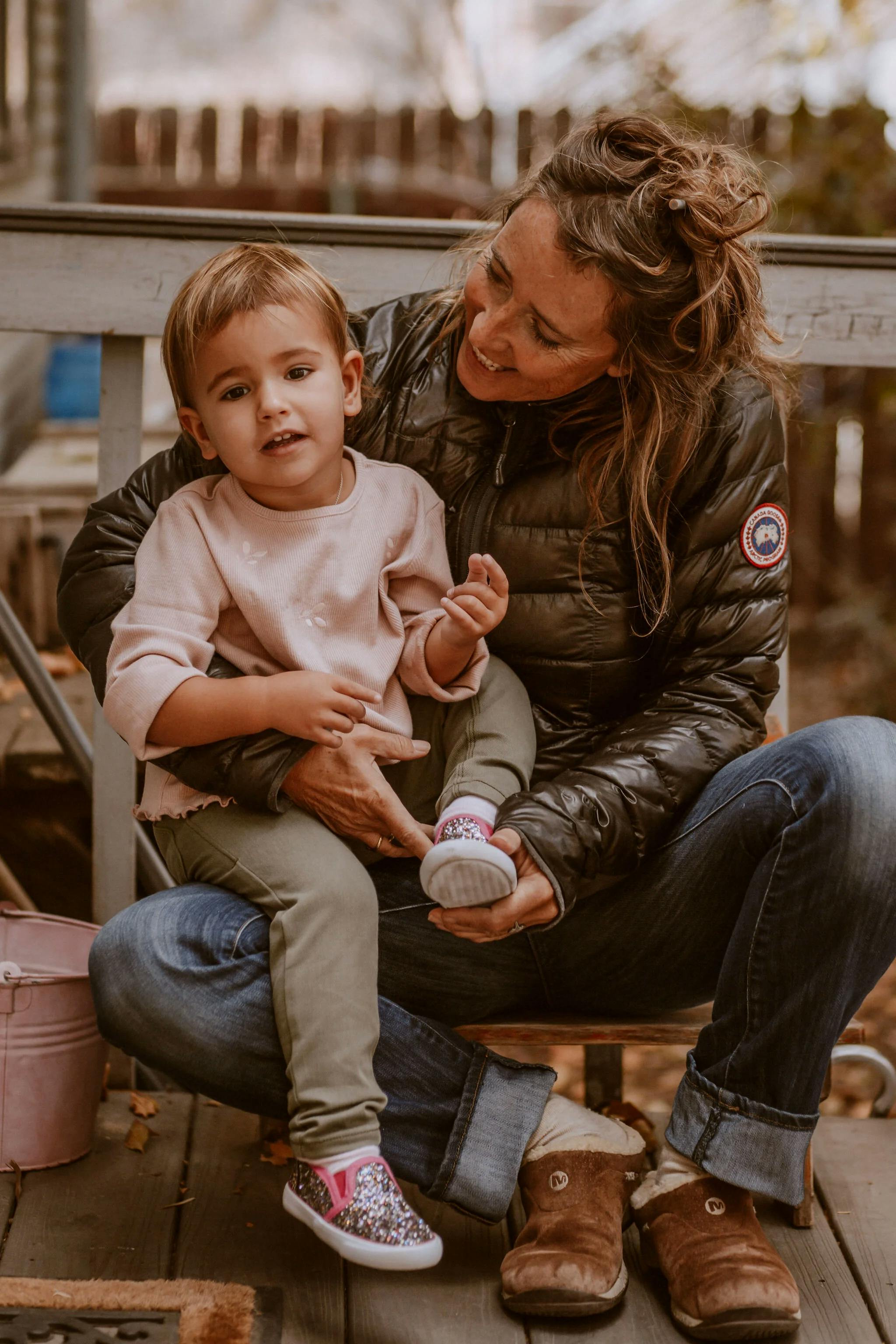 Adult helping a child put on a shoe while sitting on a porch