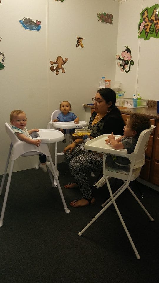 Person with three children in high chairs in a room with animal wall decals
