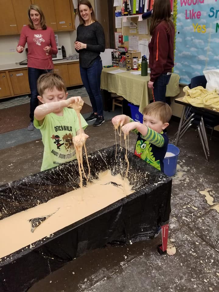 Two children playing with a gooey substance in a long black bin
