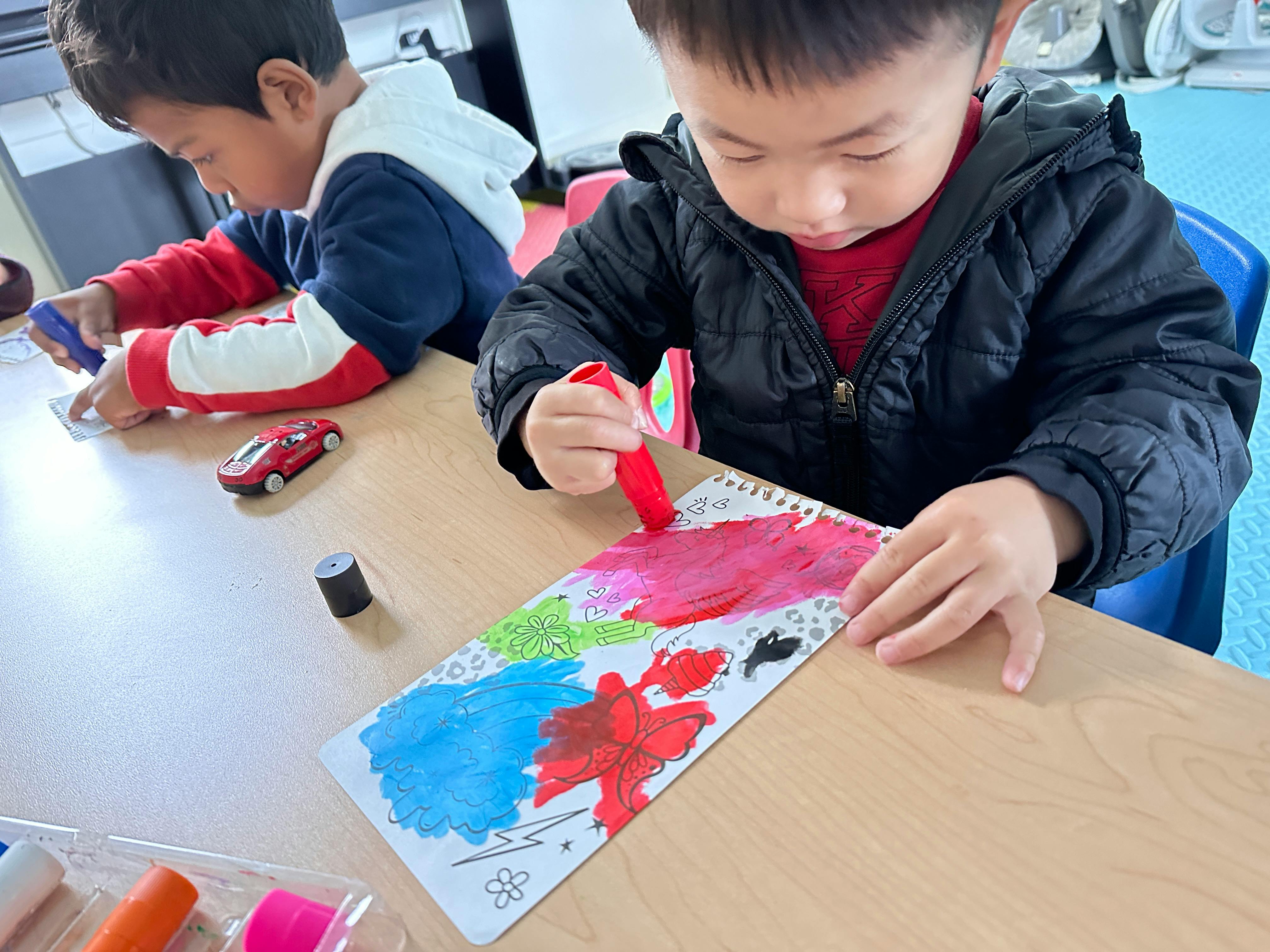 Child painting on paper with another child in the background