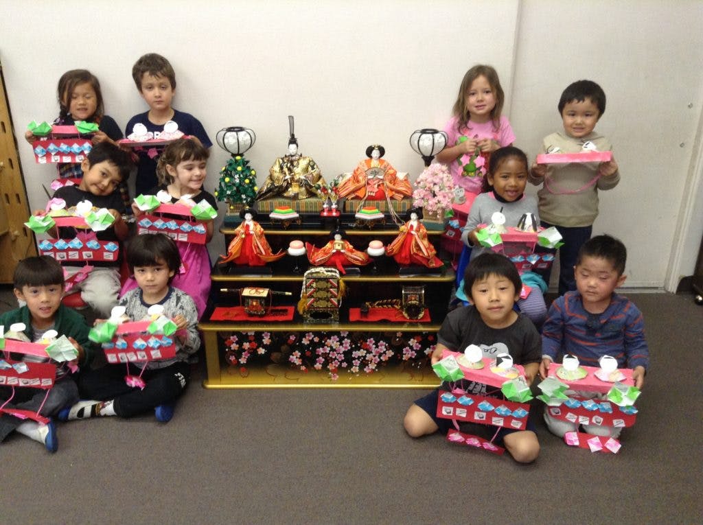 Children holding crafts in front of a display of traditional dolls
