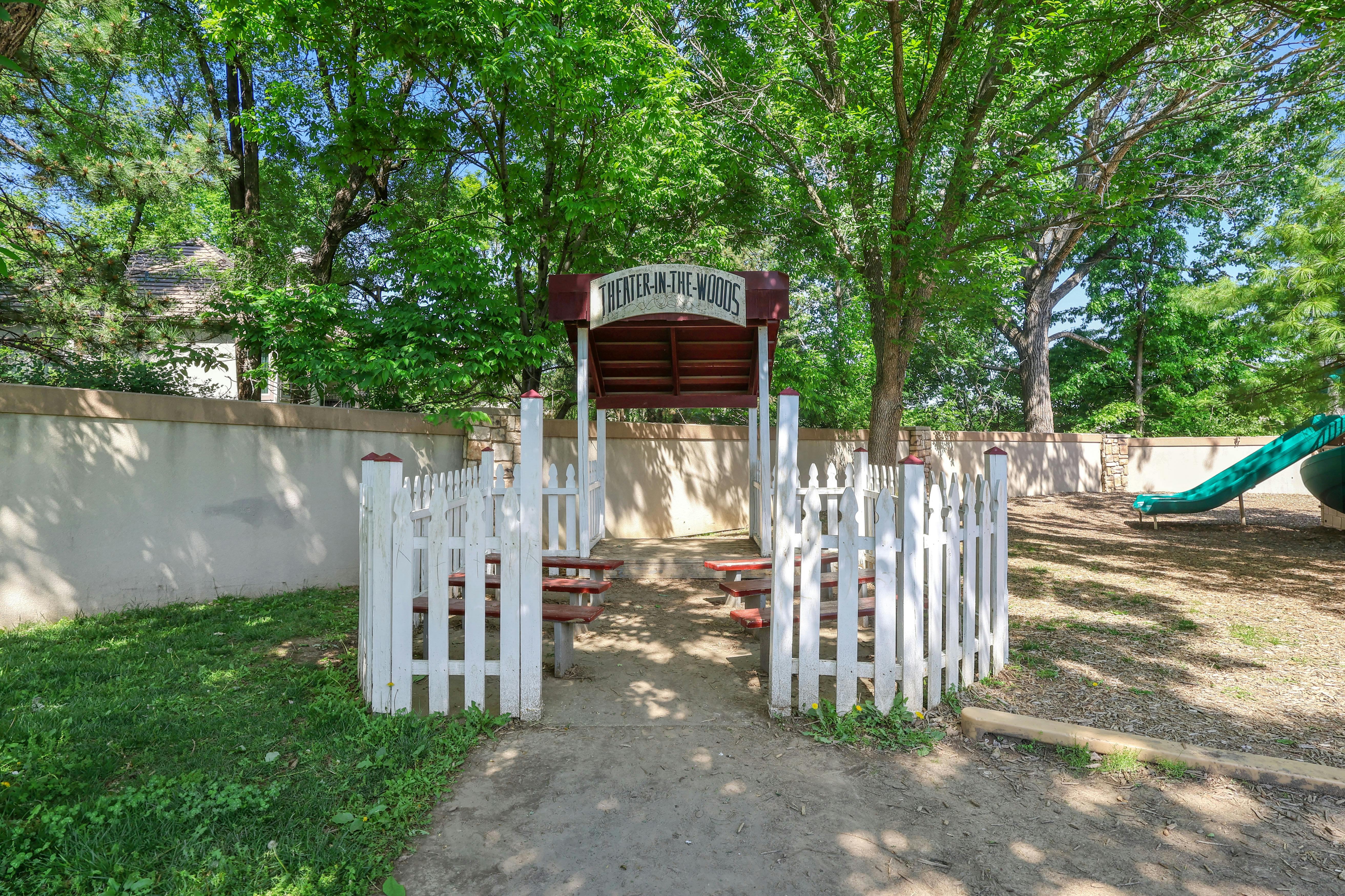 Sign that reads "THEATER-IN-THE-WOODS" over a small stage with benches
