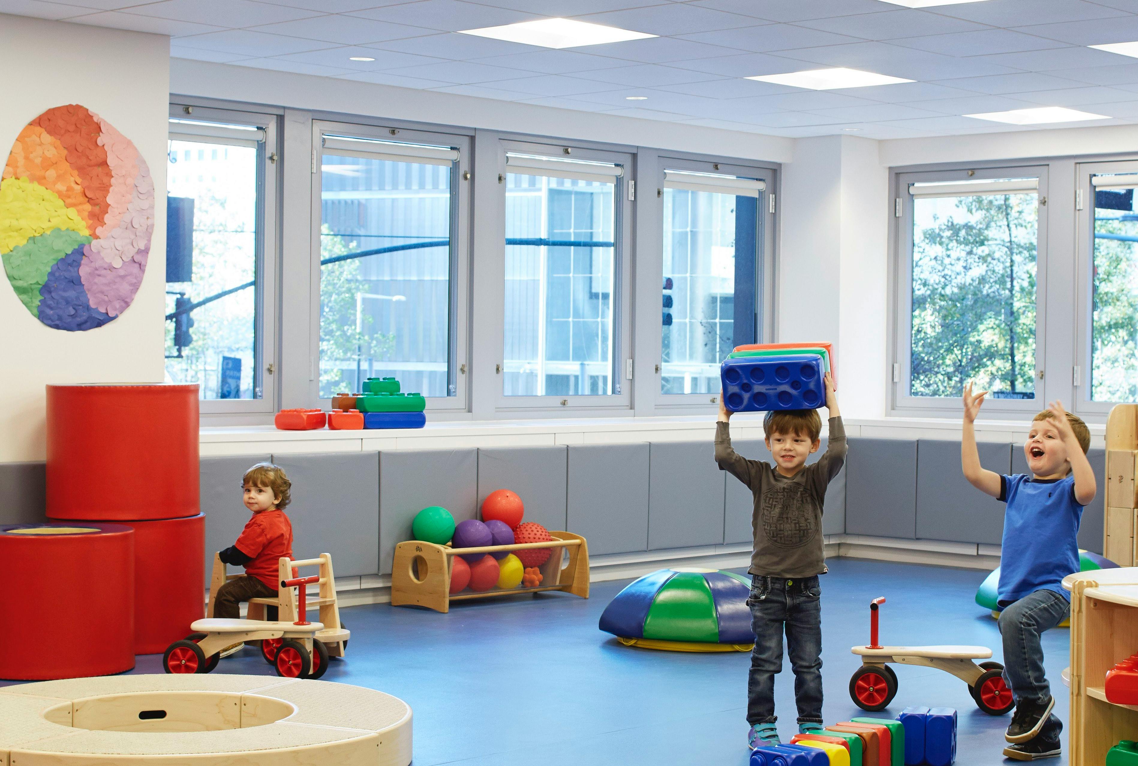 Three children playing in a room with toys and large windows