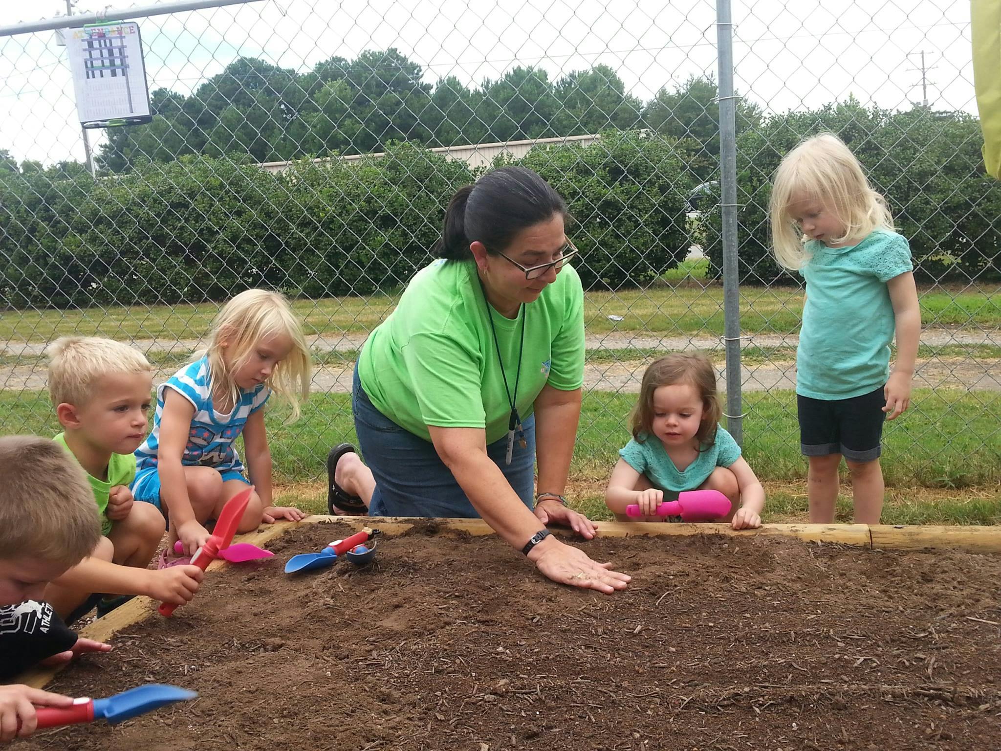 Person and children planting in a garden bed