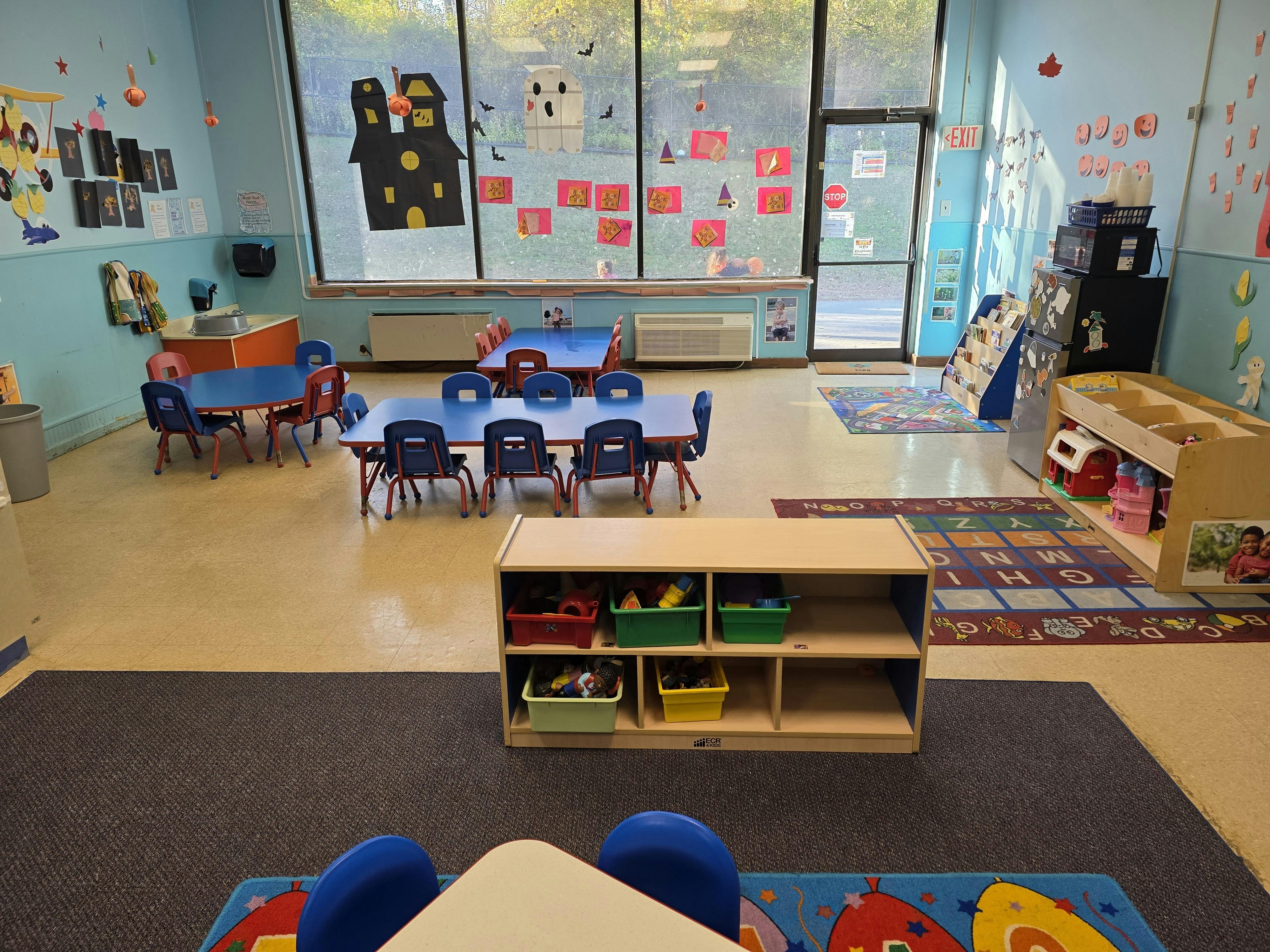 Empty classroom with small blue tables and chairs, Halloween decorations on windows