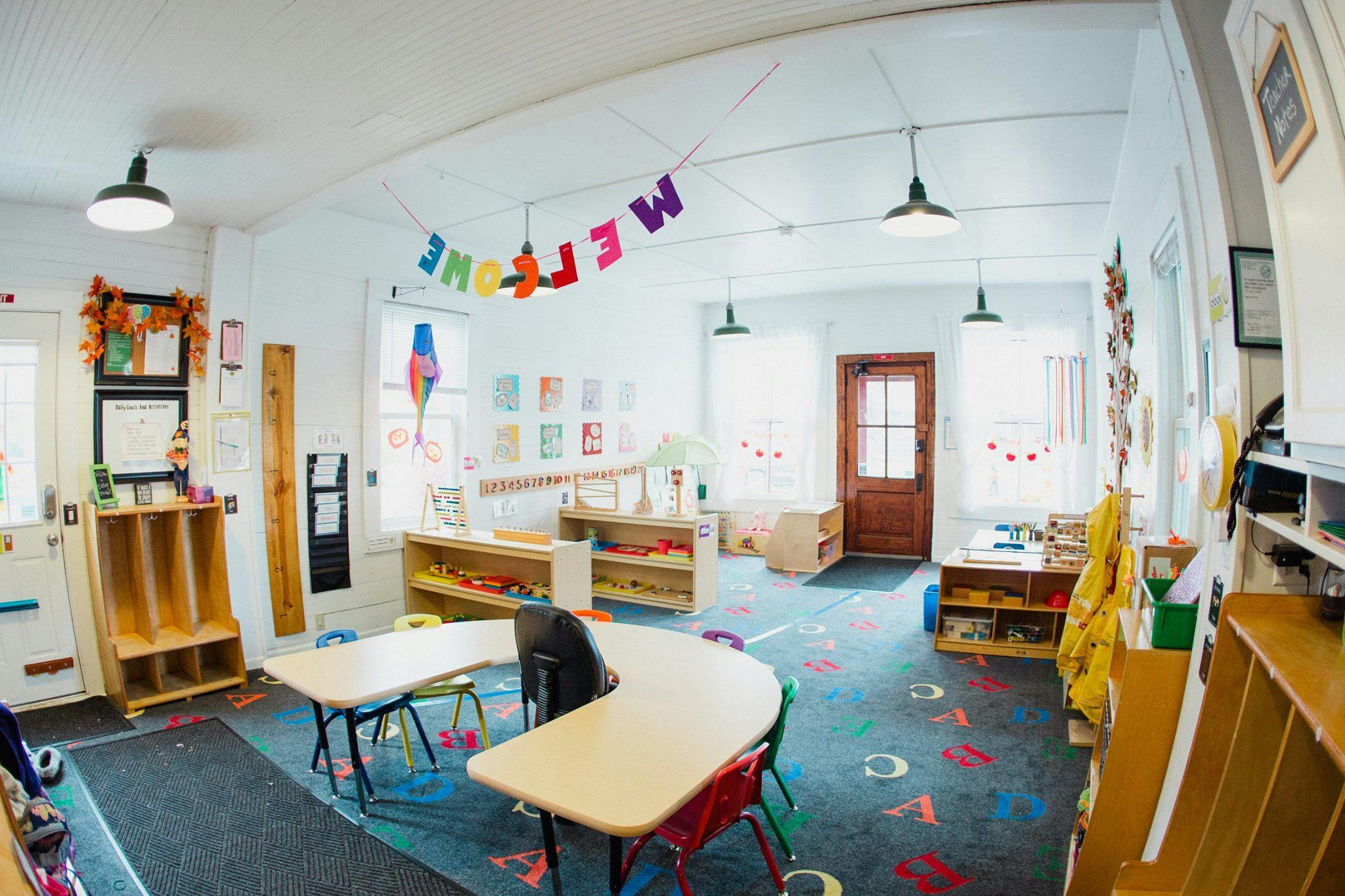 Empty classroom with small tables and chairs, shelves, and a colorful banner