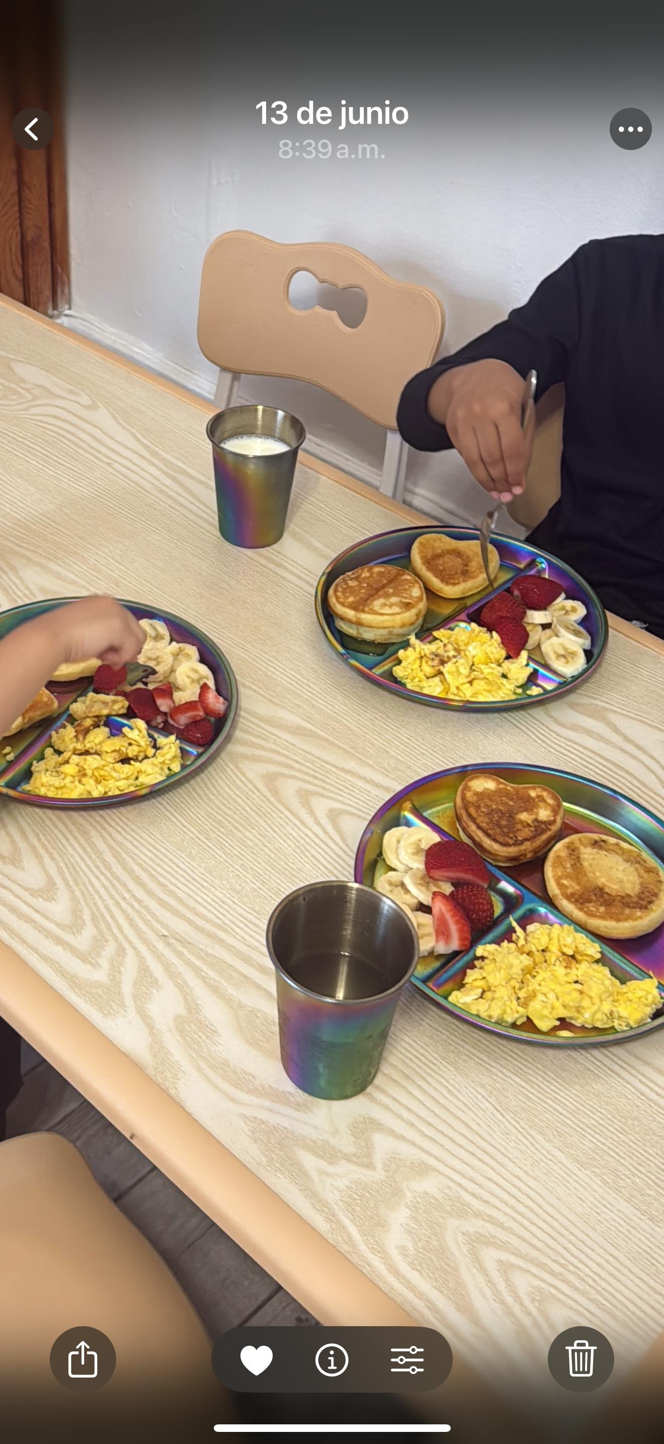 People eating pancakes with fruit and scrambled eggs at a wooden table