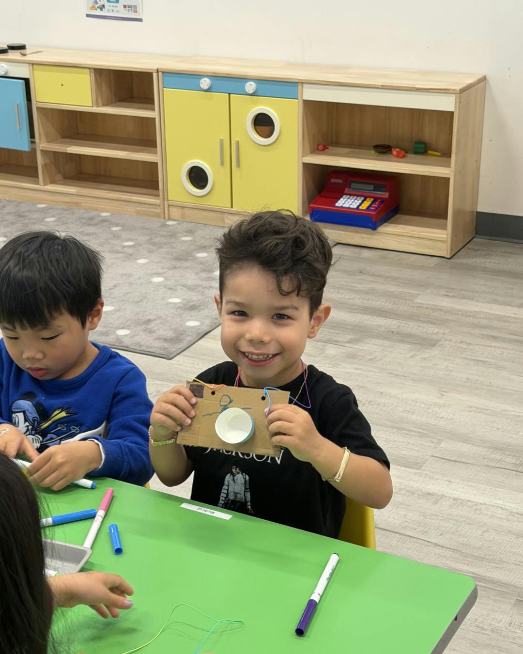 Child in a classroom holding up a cardboard craft camera
