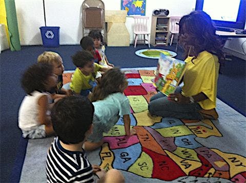 Person reading a book to a group of children in a classroom