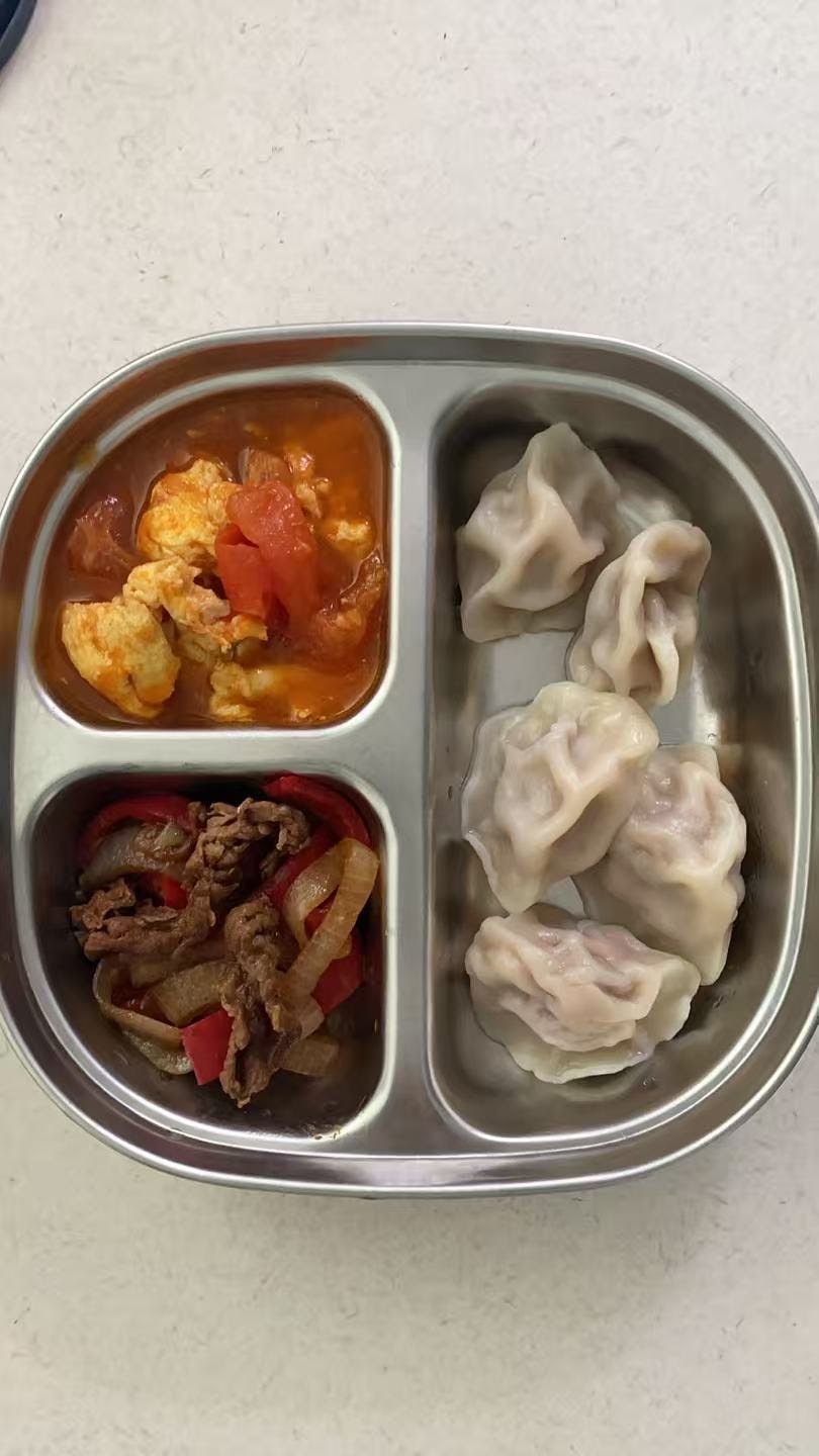 Compartmentalized metal tray containing dumplings with tomato eggs and stir-fry