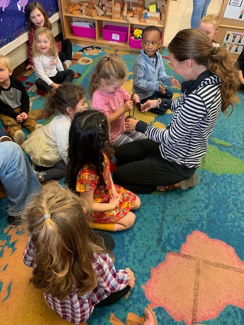 Adult and children sitting on a rug, interacting with the adult showing an object to a child