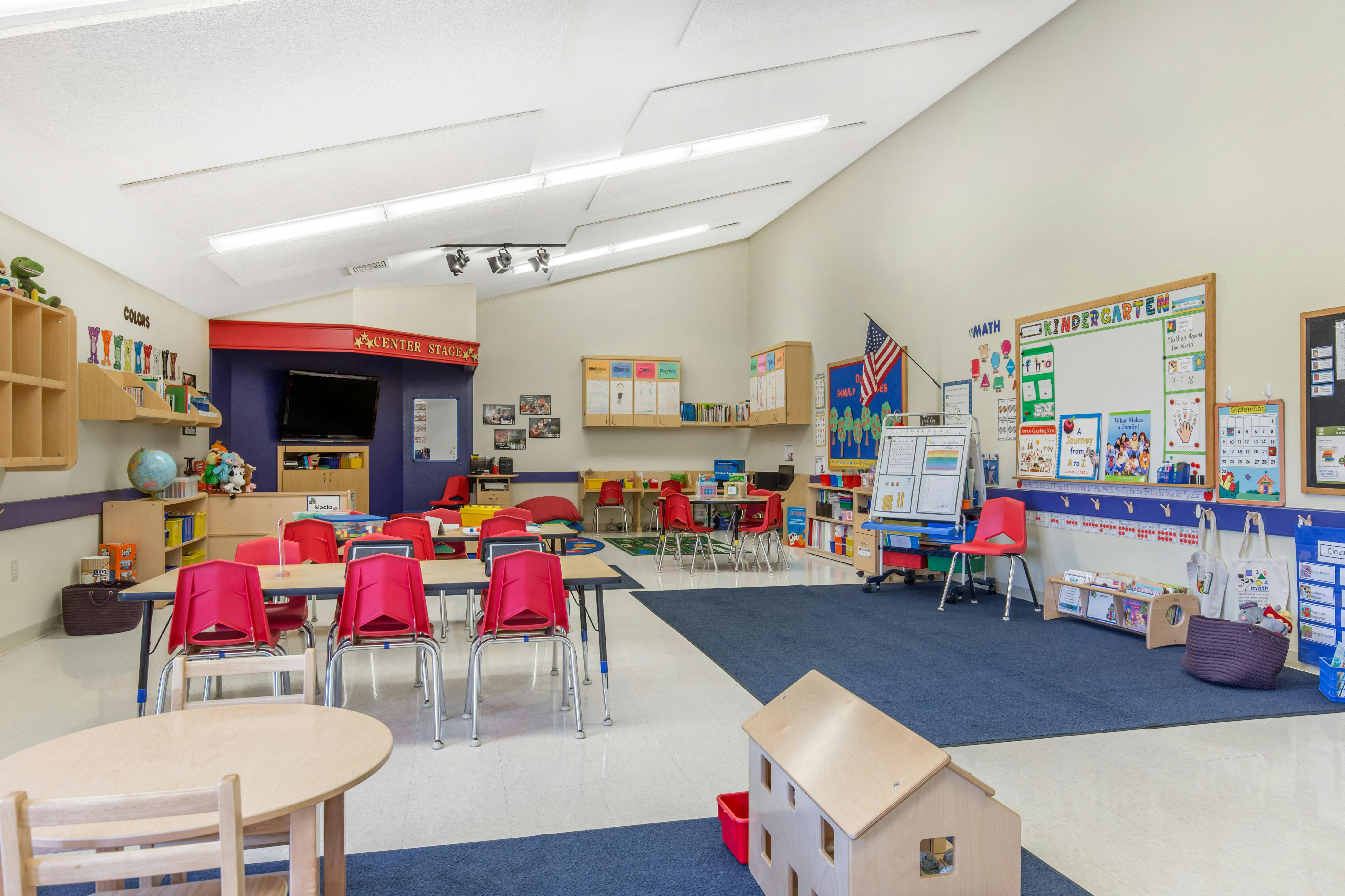 An empty kindergarten classroom with tables and red chairs