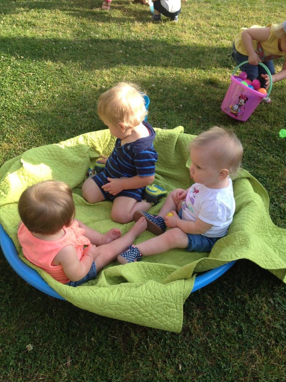 Three children sitting on a green blanket in a blue kiddie pool