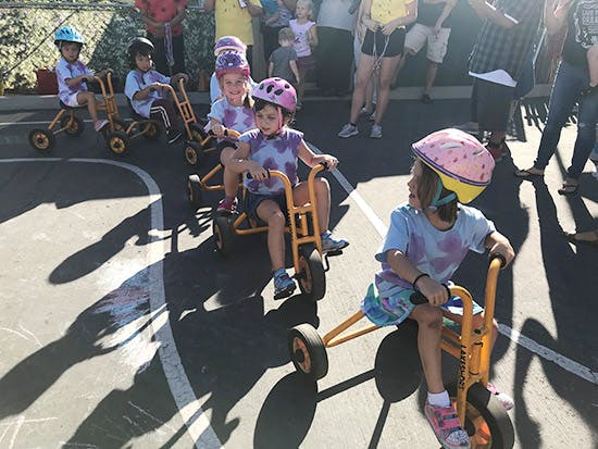 Children wearing helmets riding tricycles outdoors