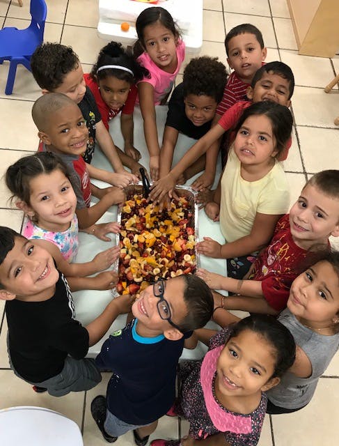 Many children gathered around a tray of fruit salad