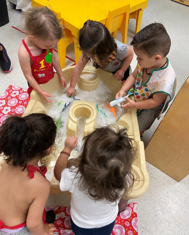 Four children playing with toys in a bubbly water table