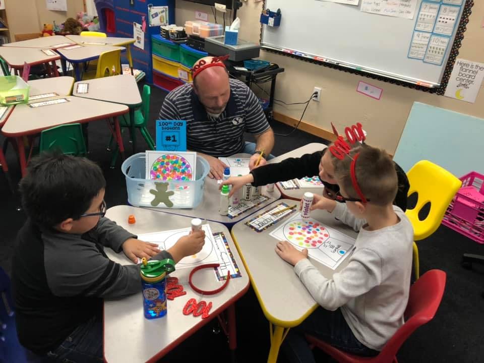 Adult and children doing crafts at a table in a classroom