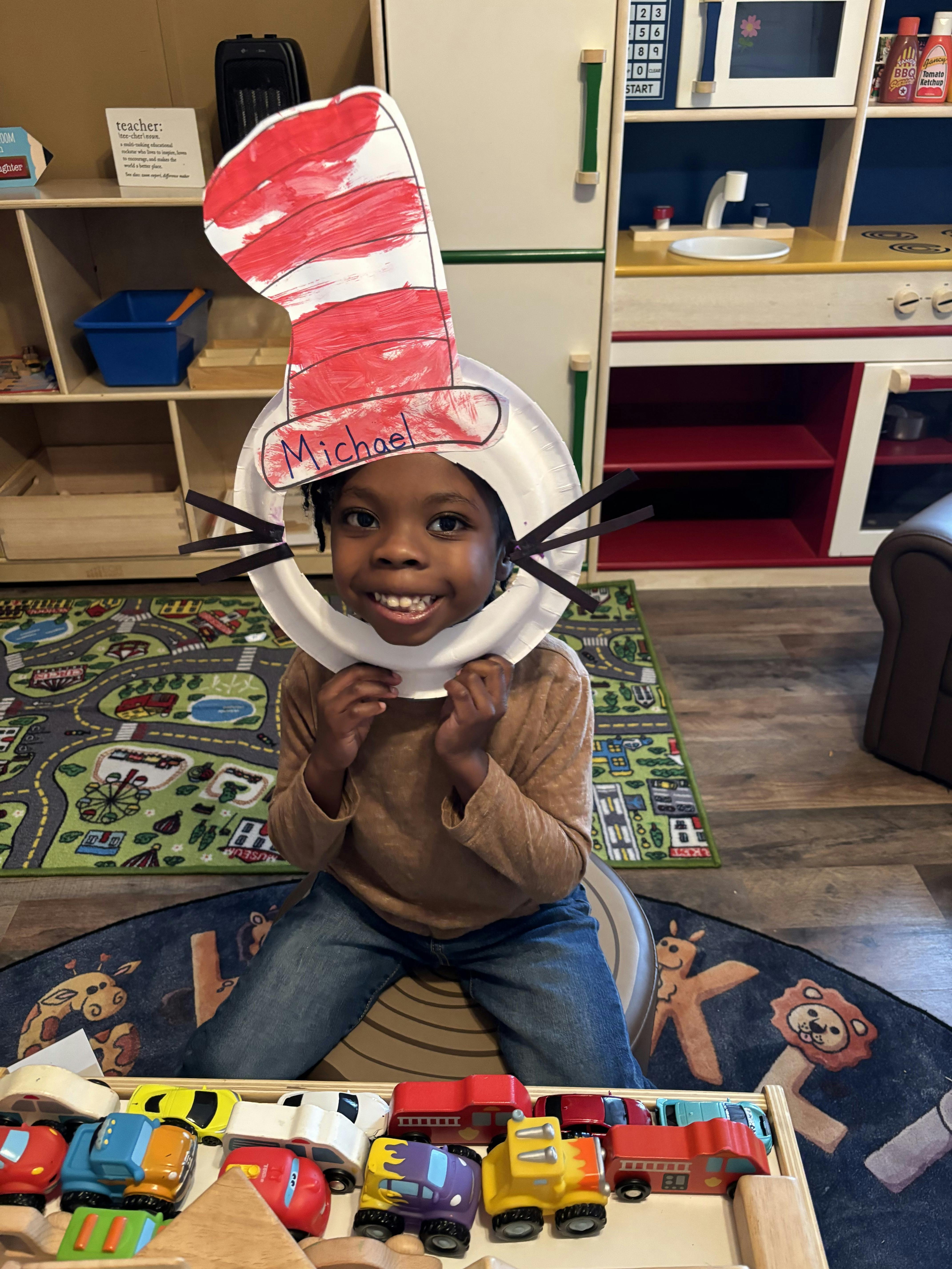 Child wearing a Cat in the Hat craft with "Michael" written on it in a classroom