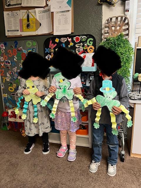Three children holding up paper leprechaun crafts