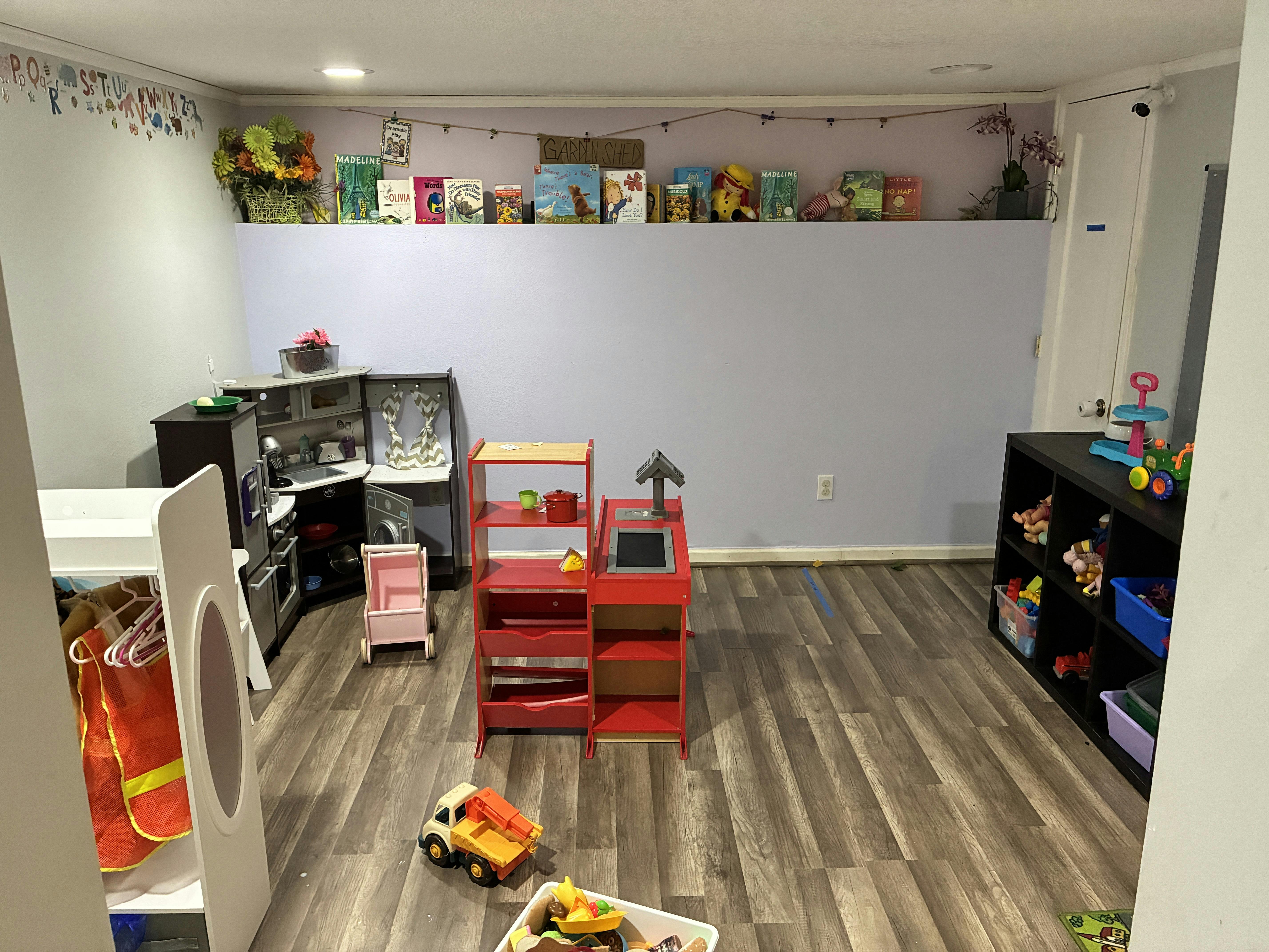 Playroom with toy kitchen, cash register, books on a shelf, and toy storage