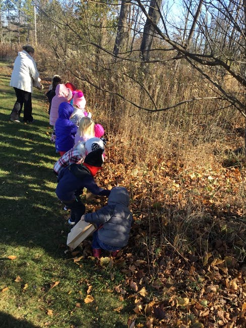 Adult and children walking in a line next to a wooded area