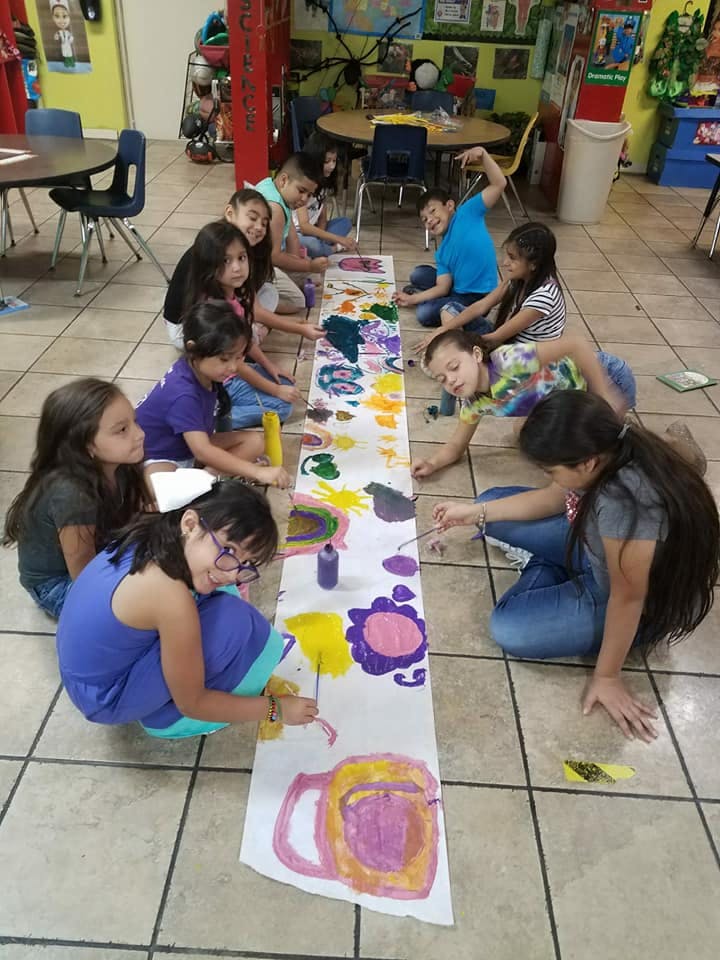 Children painting on a long sheet of paper on the floor
