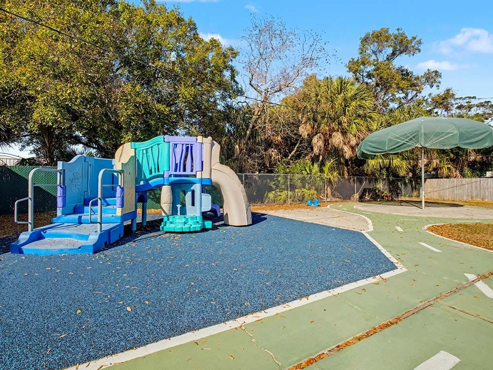 Playground with blue and purple play structure, gray slide, green umbrella