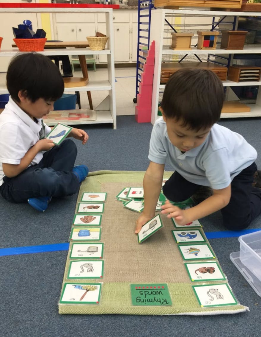 Two children playing a matching game with cards on a mat in a classroom