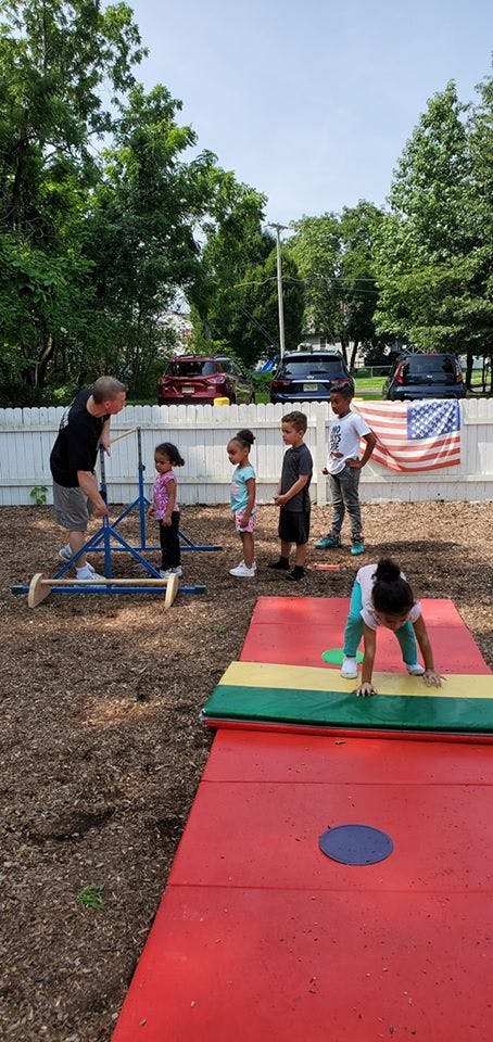 Adult and children on an outdoor play area with mats and American flag