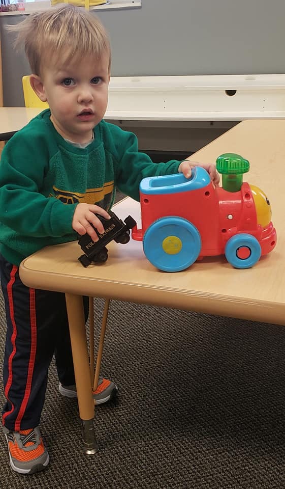Child standing at a table playing with a toy train