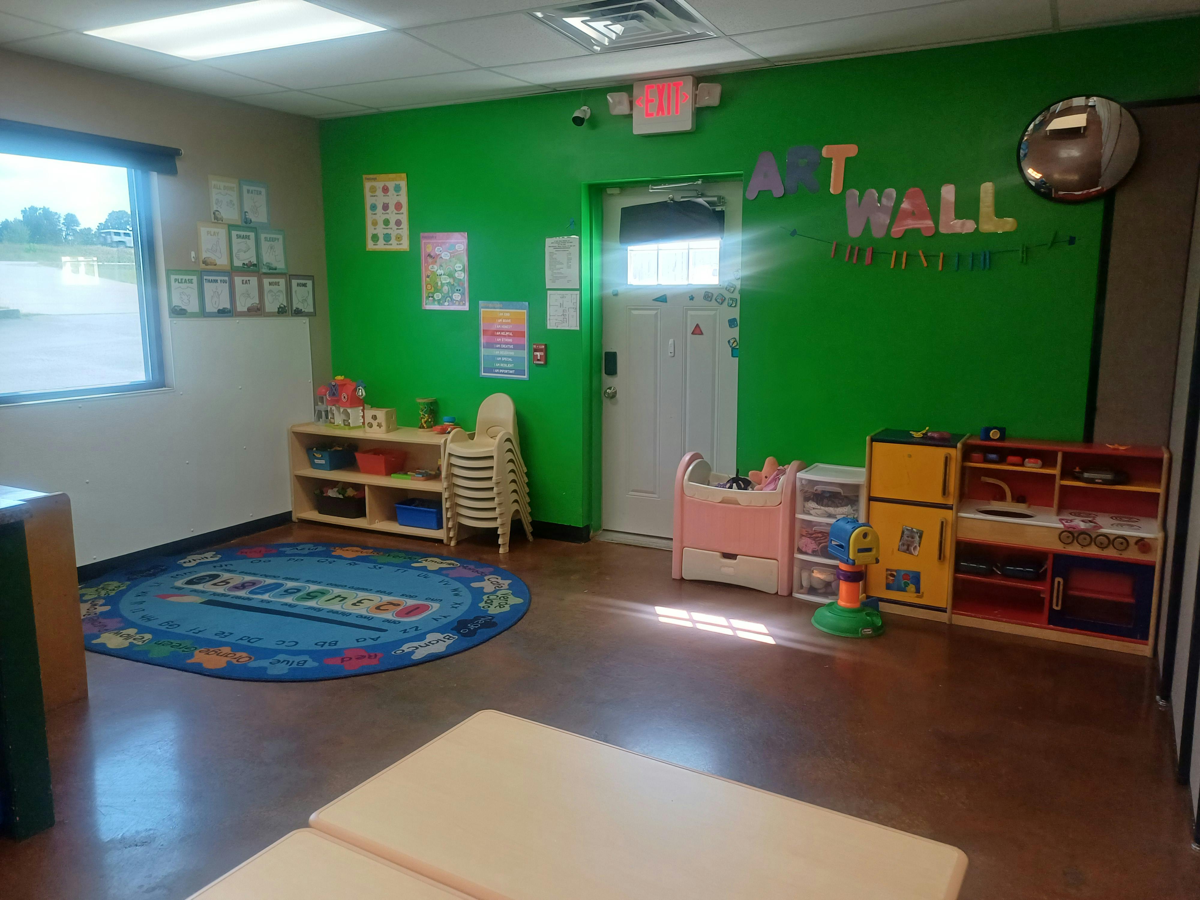 Classroom with green wall, door, window, rug, and shelves with toys