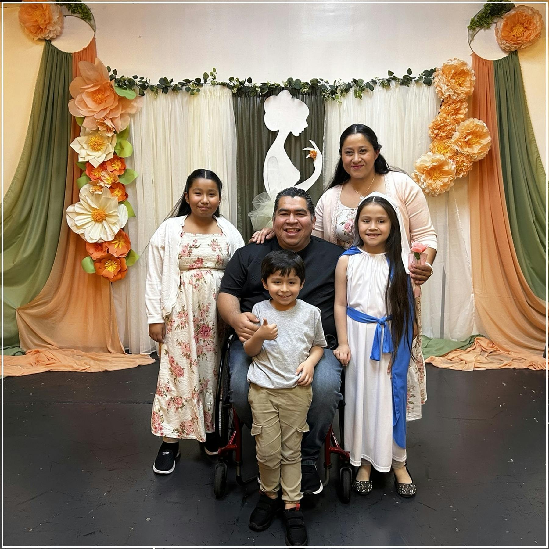 A family of five posing for a photo in front of a decorated floral backdrop