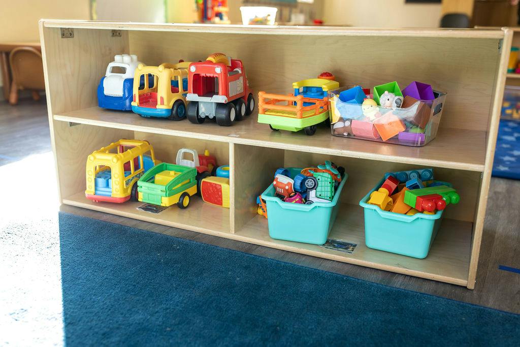 Wooden shelving unit stocked with various plastic toy vehicles and storage bins