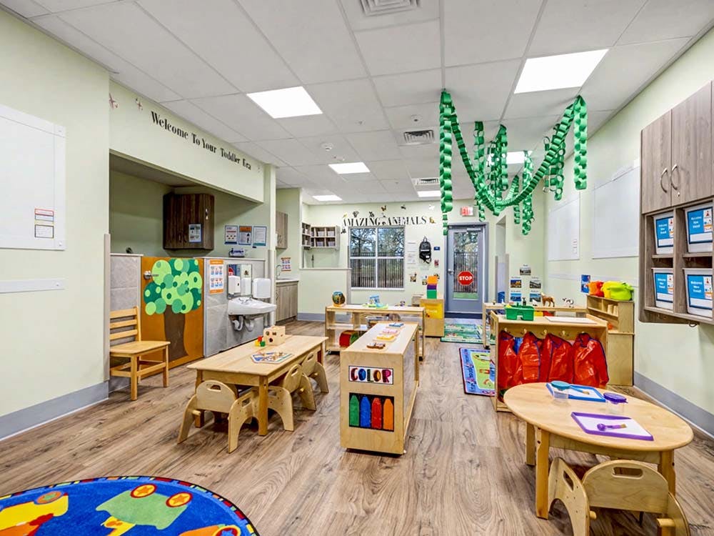 Empty toddler classroom with small tables, chairs, and play areas