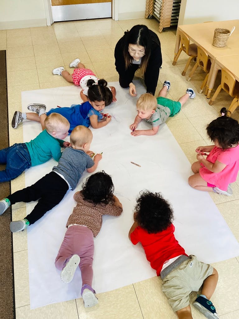 A teacher and children lying on the floor drawing together on a large paper roll