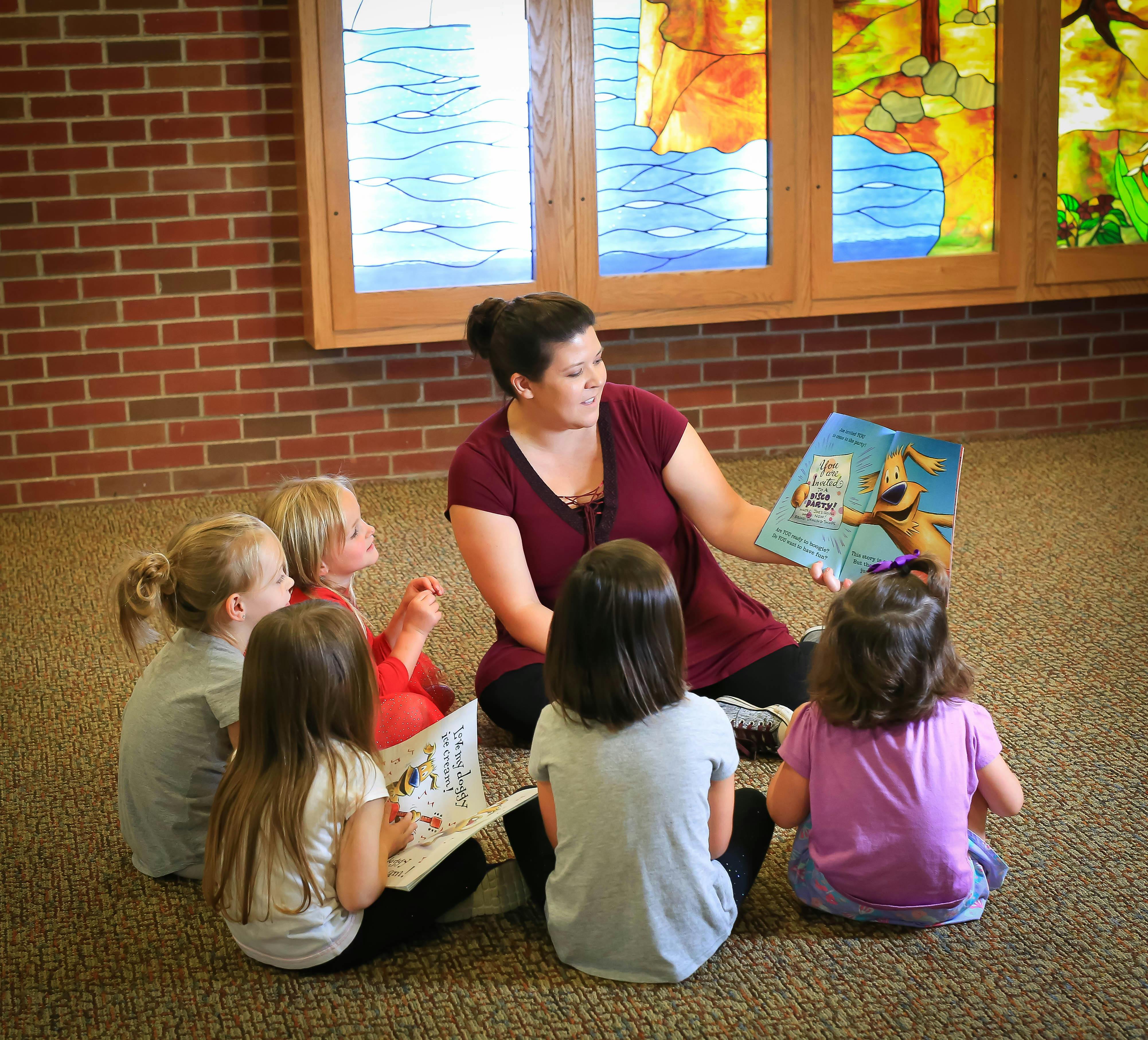 Adult reading a book to a group of children sitting on the floor