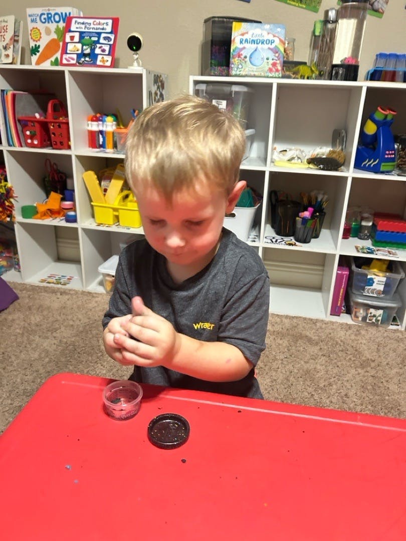 Child playing with a small container on a red table