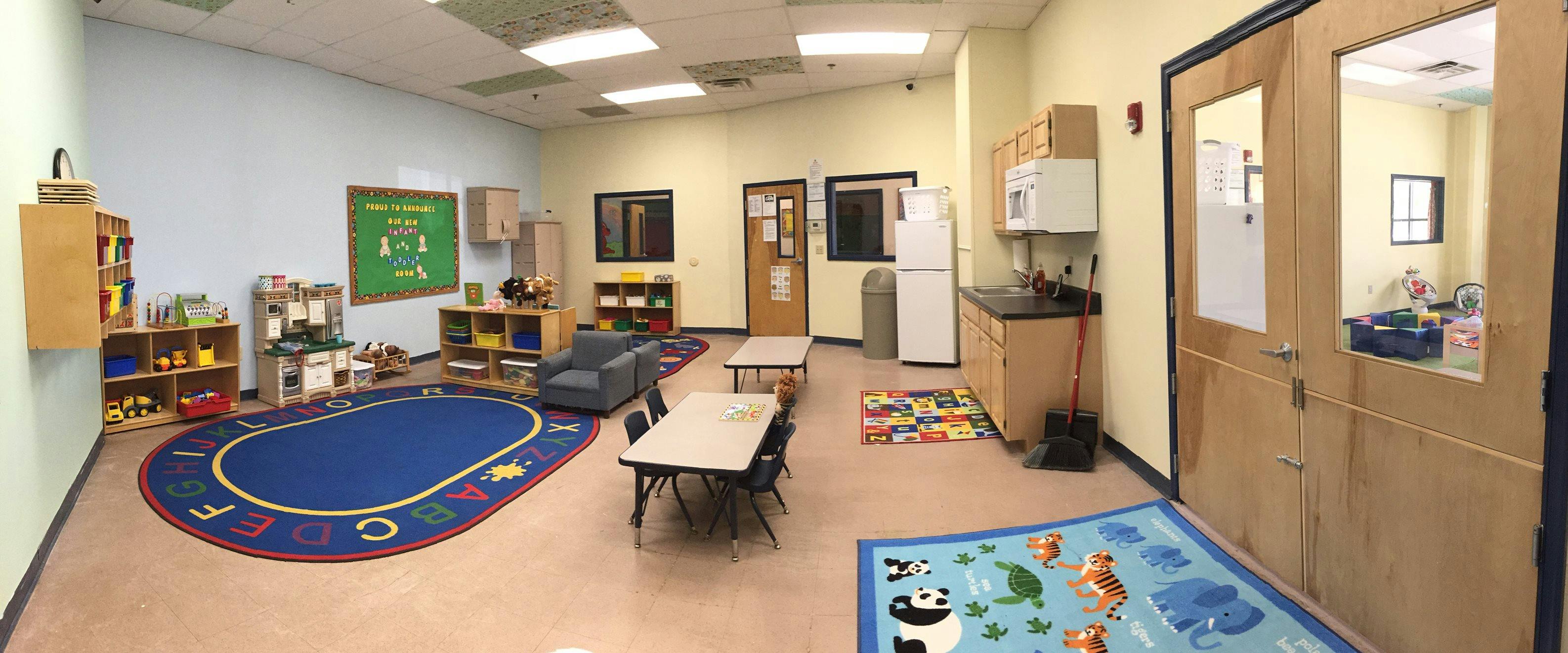 Classroom with a blue oval rug, small tables, and a play kitchen