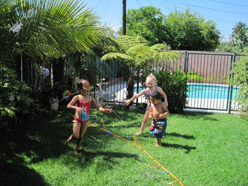 Three children playing with a sprinkler in a grassy yard