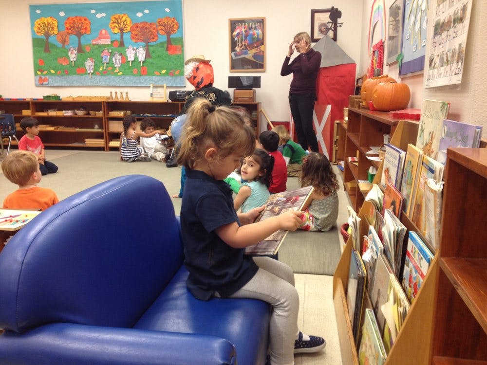 Child sitting on blue chair reading a book in a classroom