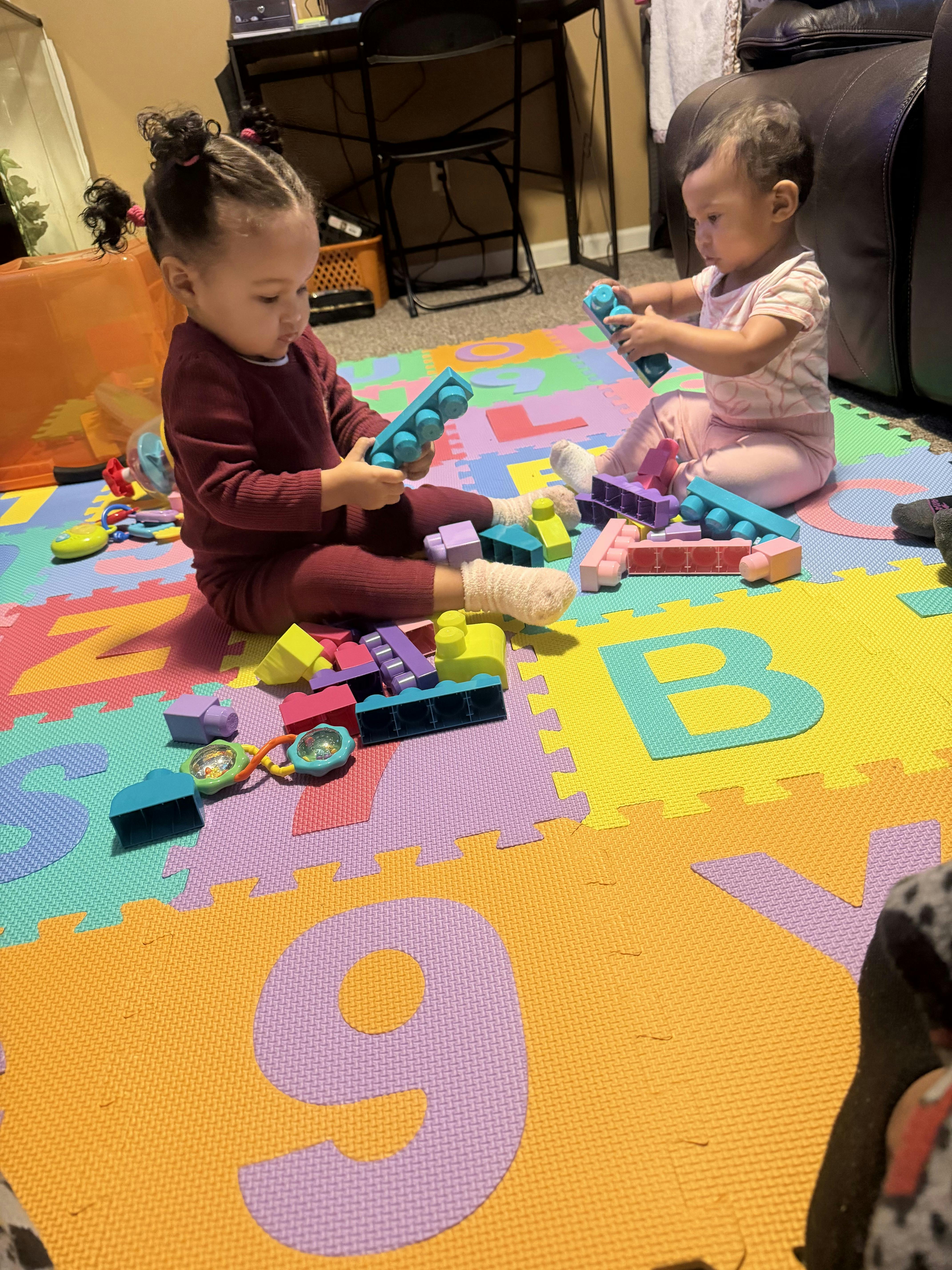 Two children sitting on a playmat, playing with building blocks