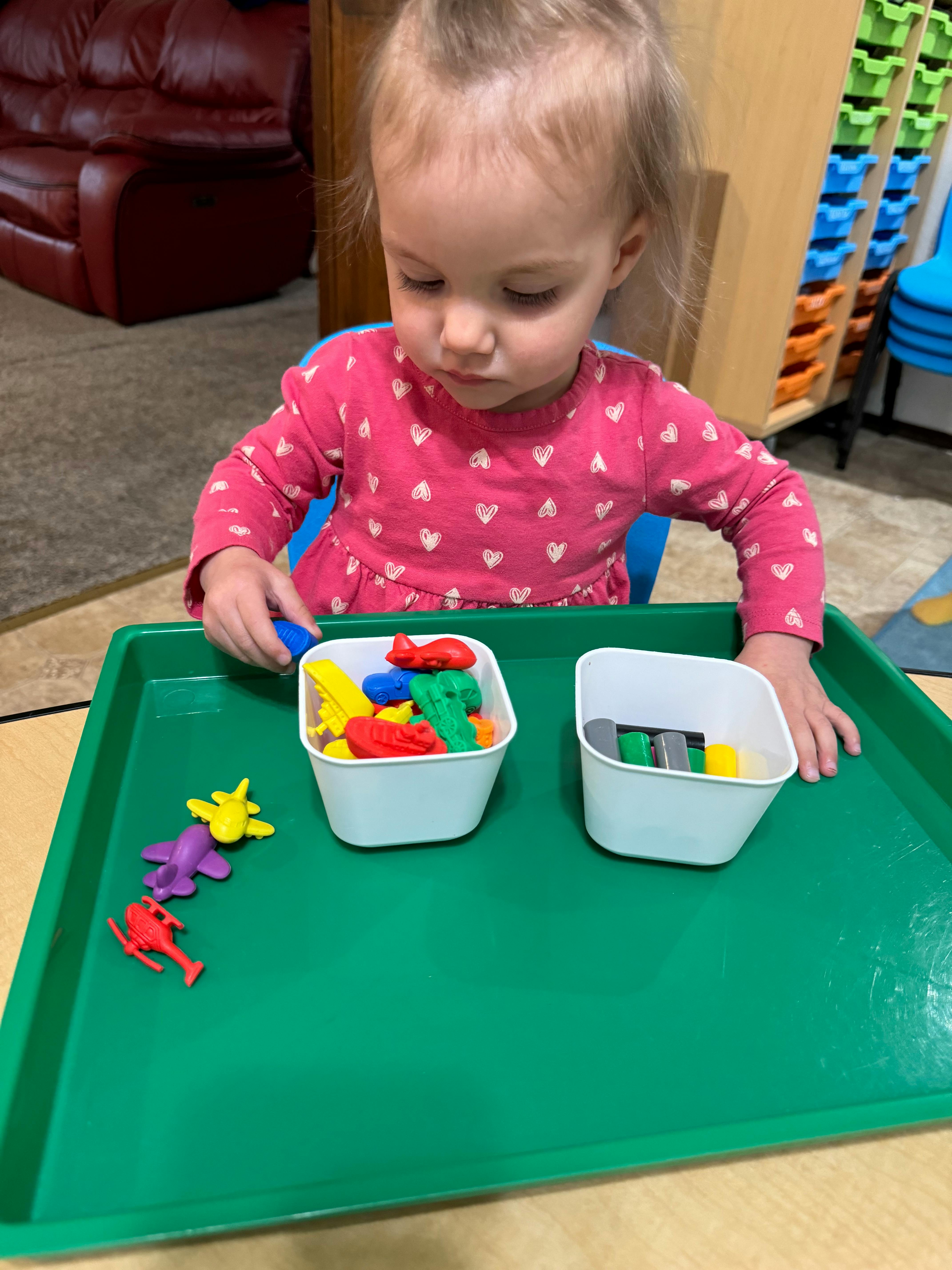 Child playing with colorful toy vehicles on a green tray