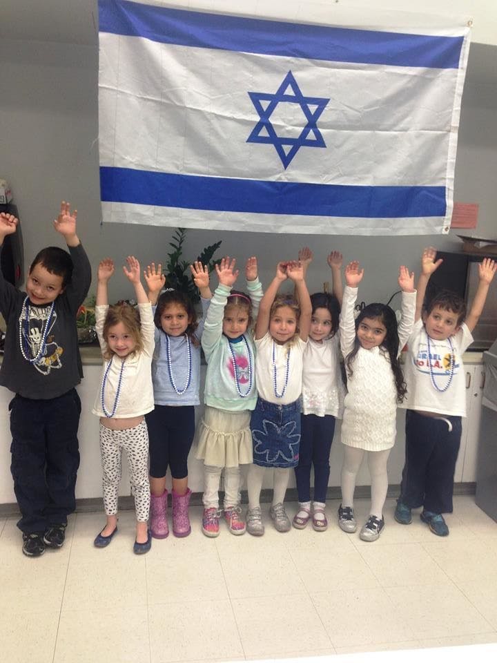 Group of children with hands raised in front of an Israeli flag