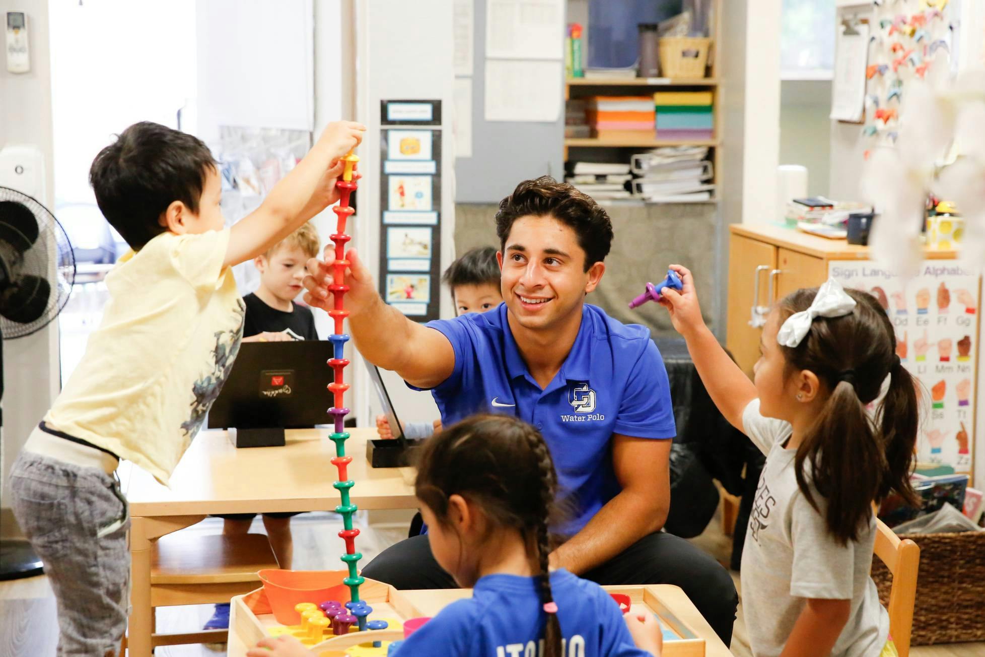 Adult and children building with colorful interlocking toys in a classroom
